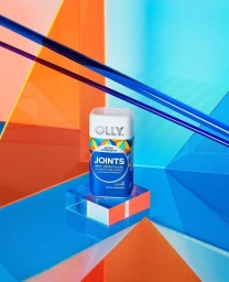 Olly Joints supplement bottle resting on a clear blue acrylic block amid colorful translucent geometric panels.