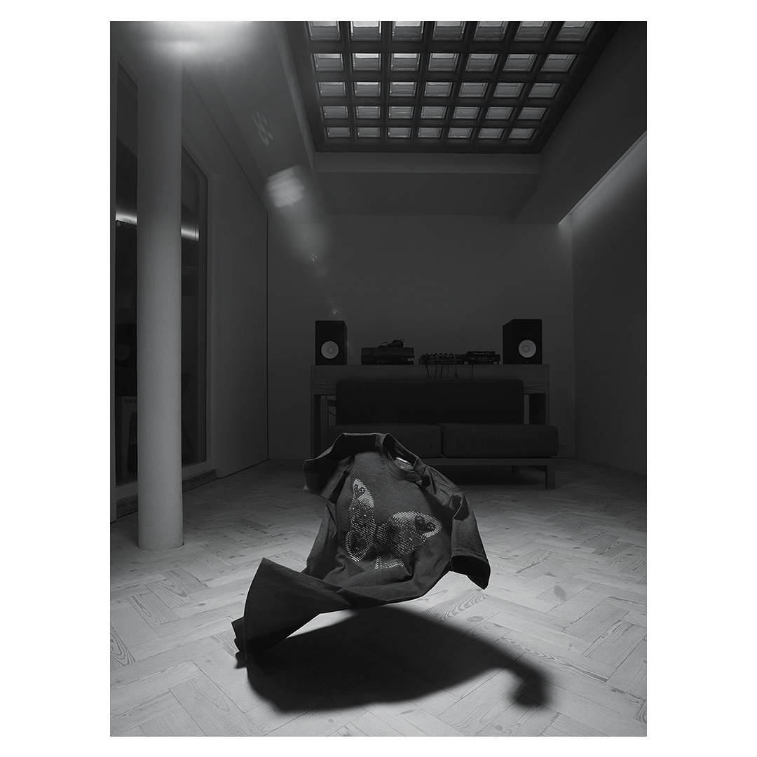Monochromatic studio shot of a dark shirt with a butterfly design floating mid-air above a light herringbone pattern floor.