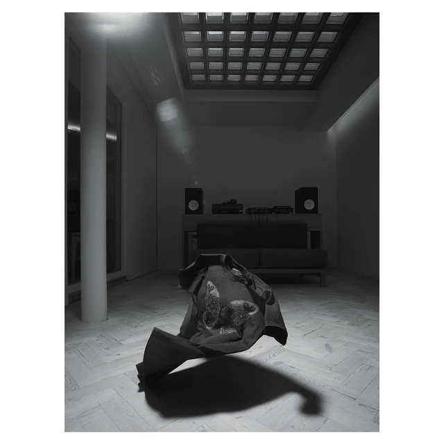 Monochromatic studio shot of a dark shirt with a butterfly design floating mid-air above a light herringbone pattern floor.