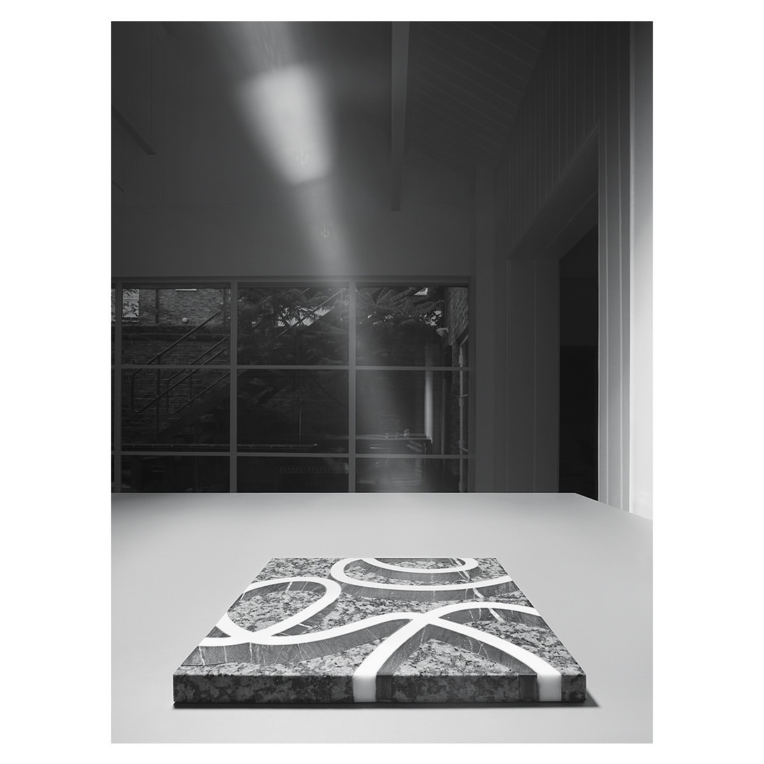 A patterned marble slab with white lines rests on a white table indoors, illuminated by a beam of light coming through a window.