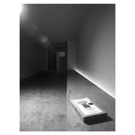 Monochromatic shot of a book titled 'Client Earth' laying on a concrete floor with a hallway in the background and subtle light.