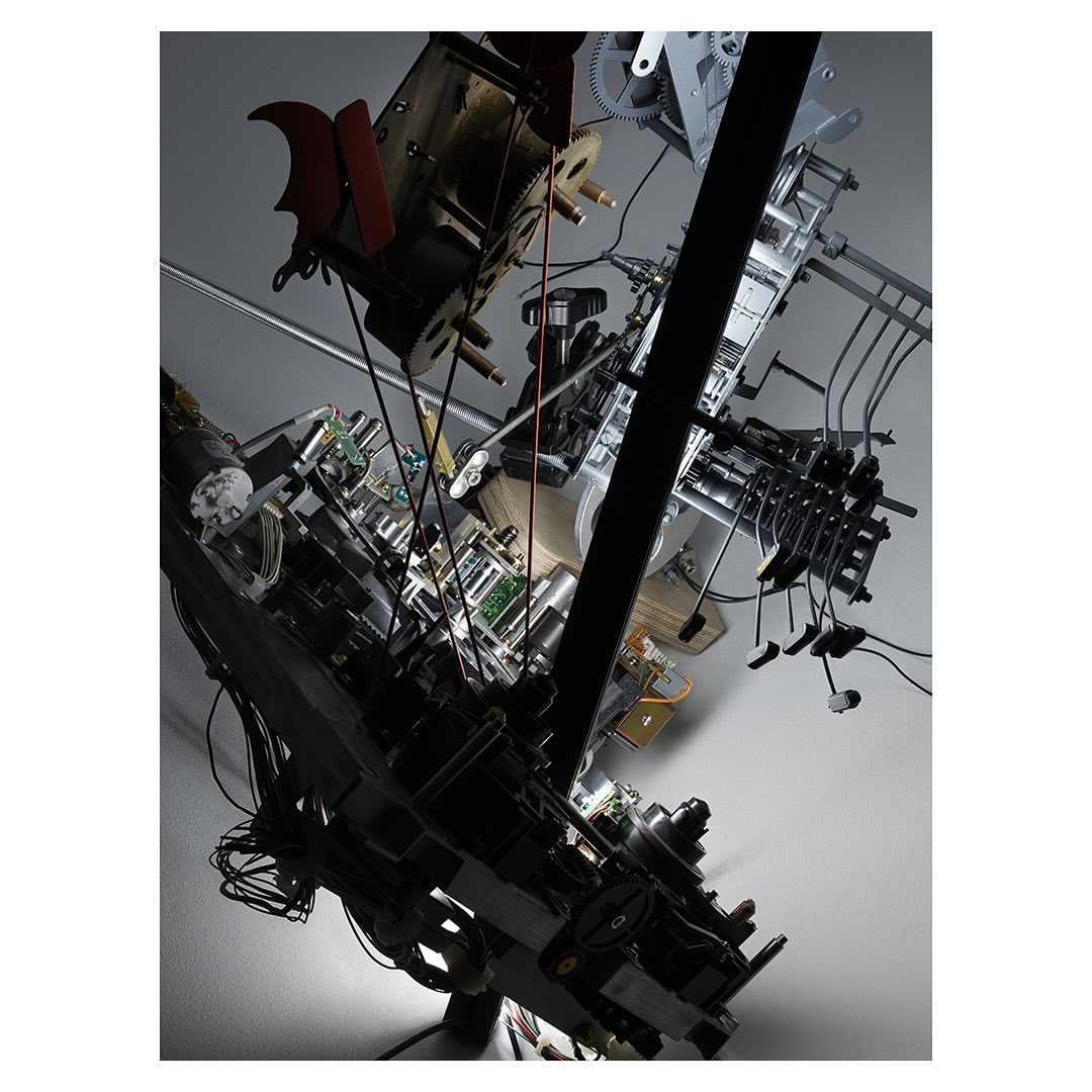 Complex industrial machinery and electrical components hanging from a ceiling with visible wires, gears, and metallic structures.