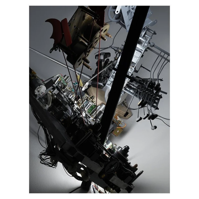 Complex industrial machinery and electrical components hanging from a ceiling with visible wires, gears, and metallic structures.
