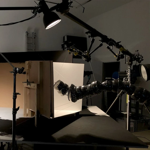 Studio shot of an object suspended by thin wires, with studio lighting and camera equipment in the background, creating a controlled environment.
