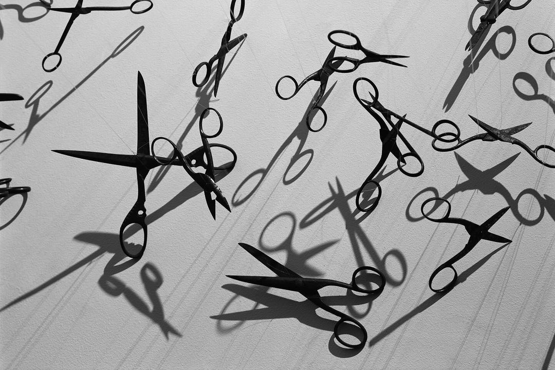 High-angle shot of multiple metal scissors, casting shadows on a bright white surface, creating a monochromatic abstract pattern.