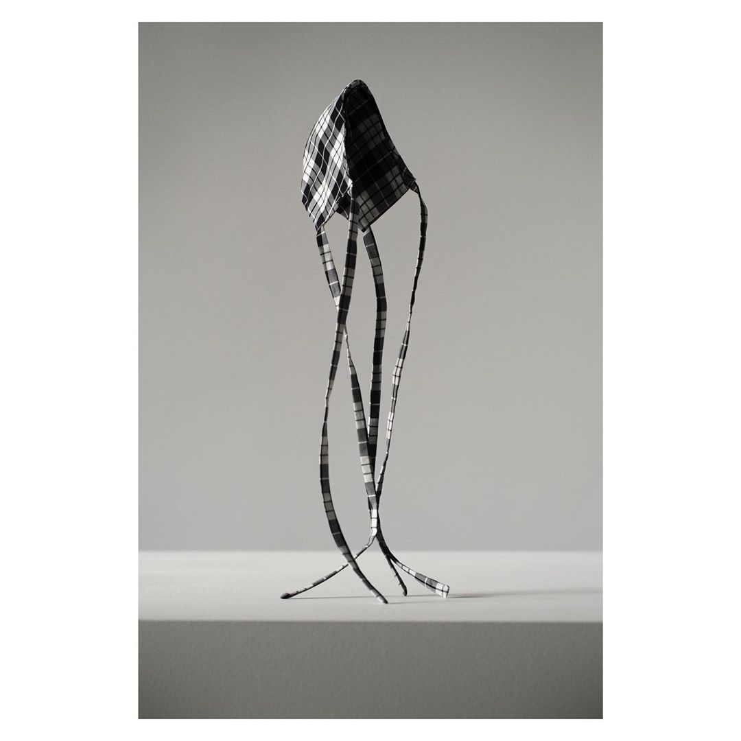 Abstract still life featuring a black and white checkered, futuristic-looking headpiece or mask, set against a solid grey backdrop.