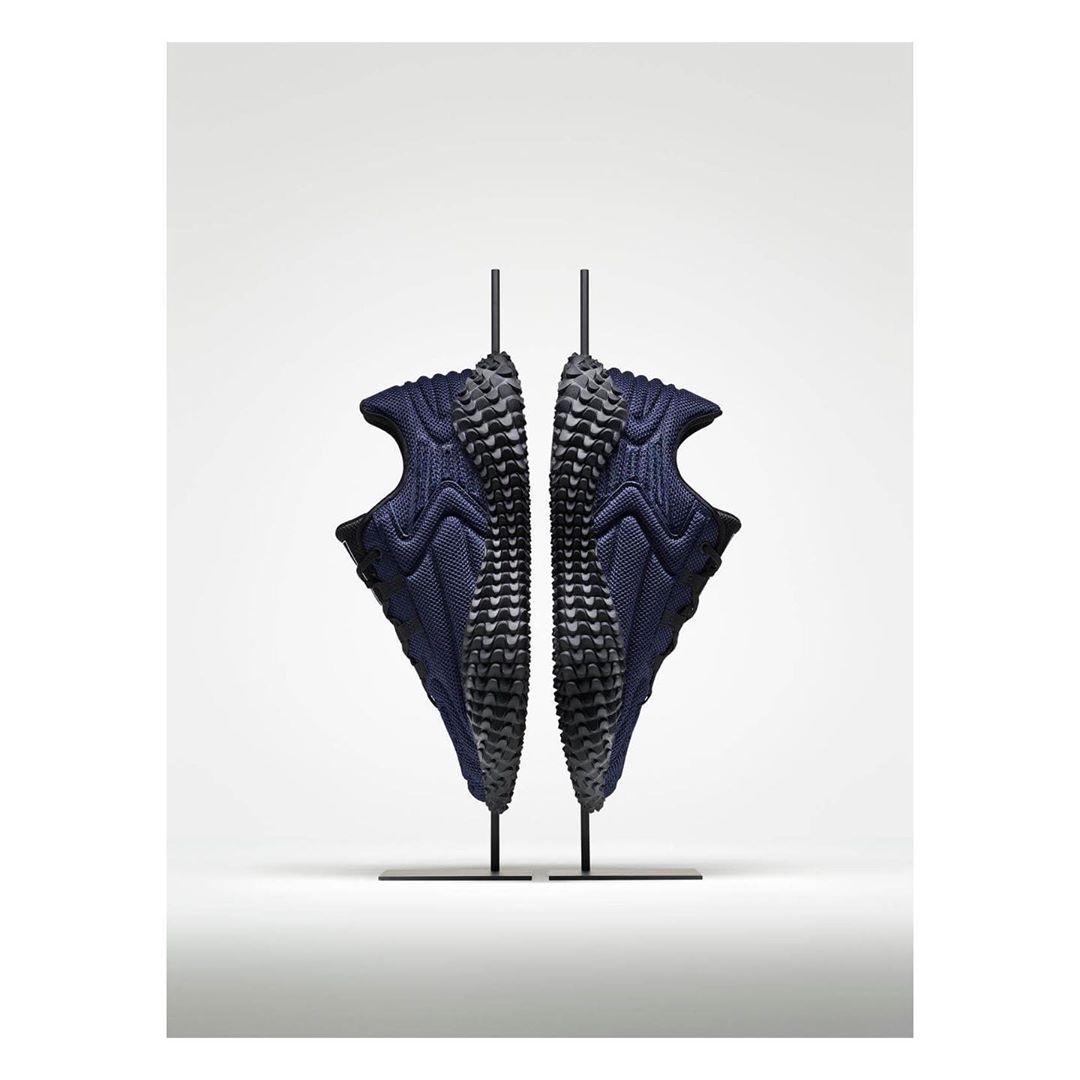 Studio shot of two athletic sneakers in dark blue, mounted on black stands with a bright white background.