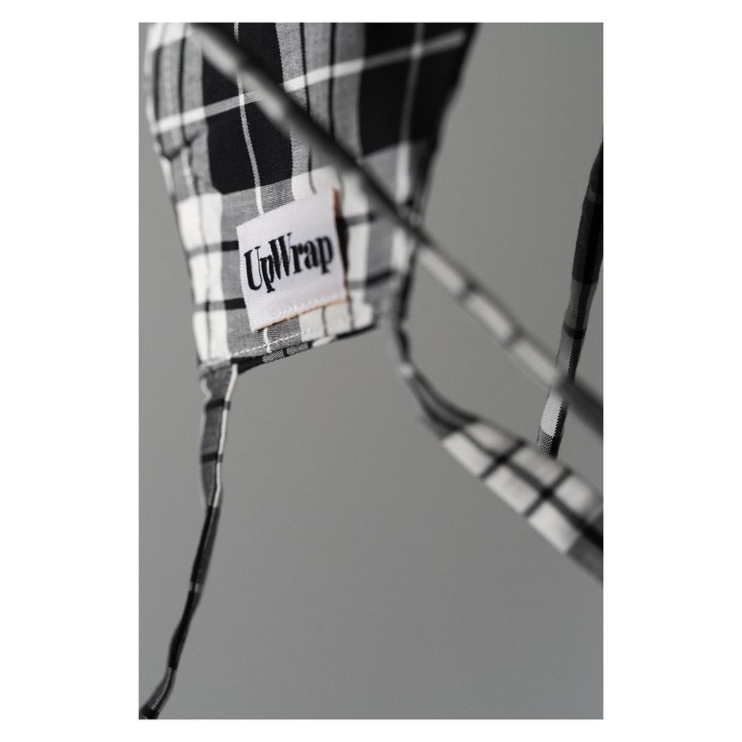 Close-up of a black-and-white plaid reusable food wrap with ties, featuring a fabric UpWrap label, against a plain grey backdrop.