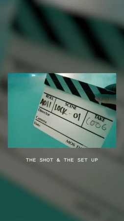 Close-up, low-angle shot of a white clapperboard with black and white stripes, marked with film details, against a blue backdrop.