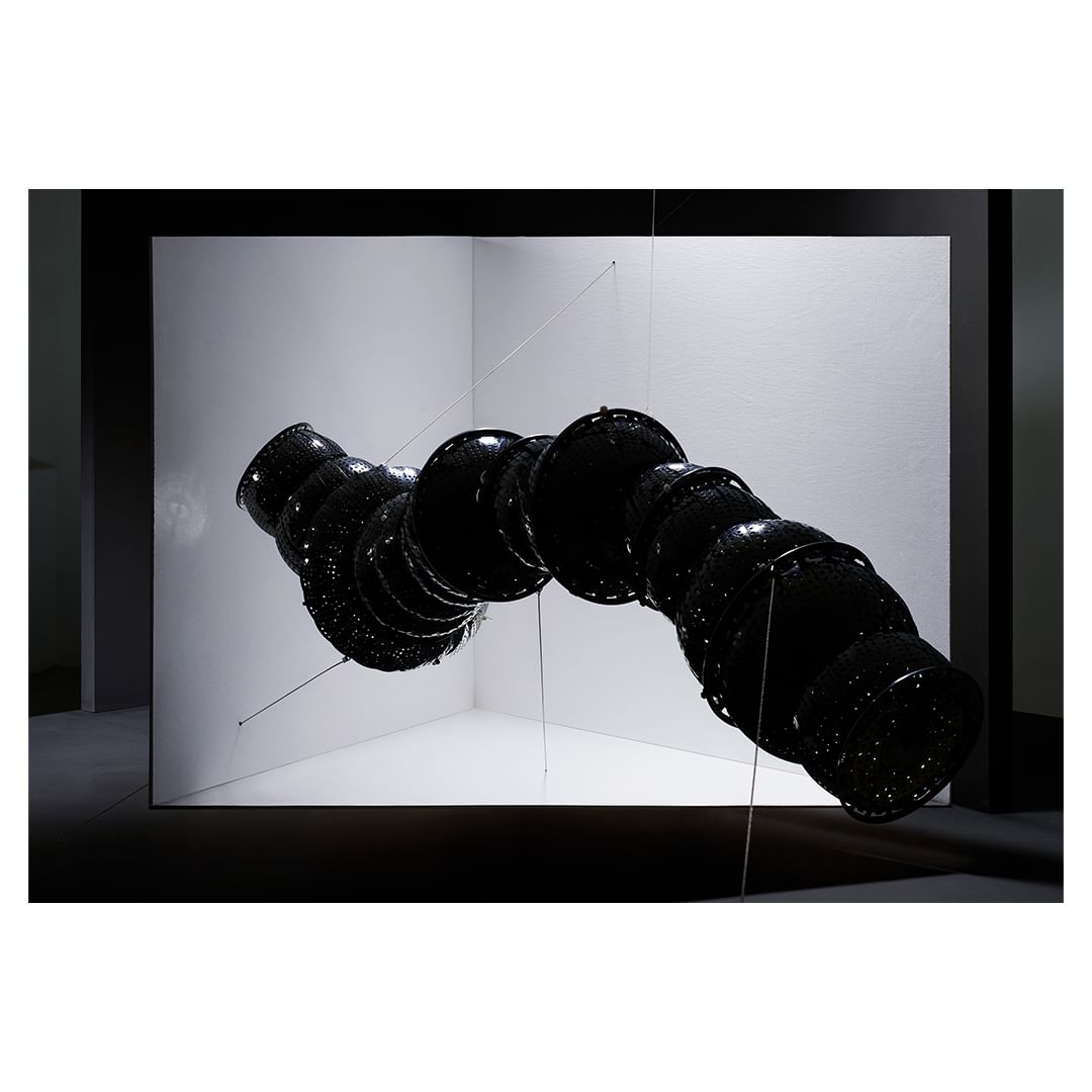 Abstract art installation with row of connected black bowls suspended in a white corner, creating a visually striking and modern display.