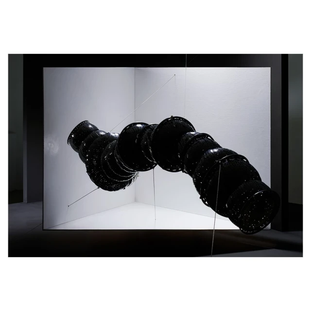 Abstract art installation with row of connected black bowls suspended in a white corner, creating a visually striking and modern display.