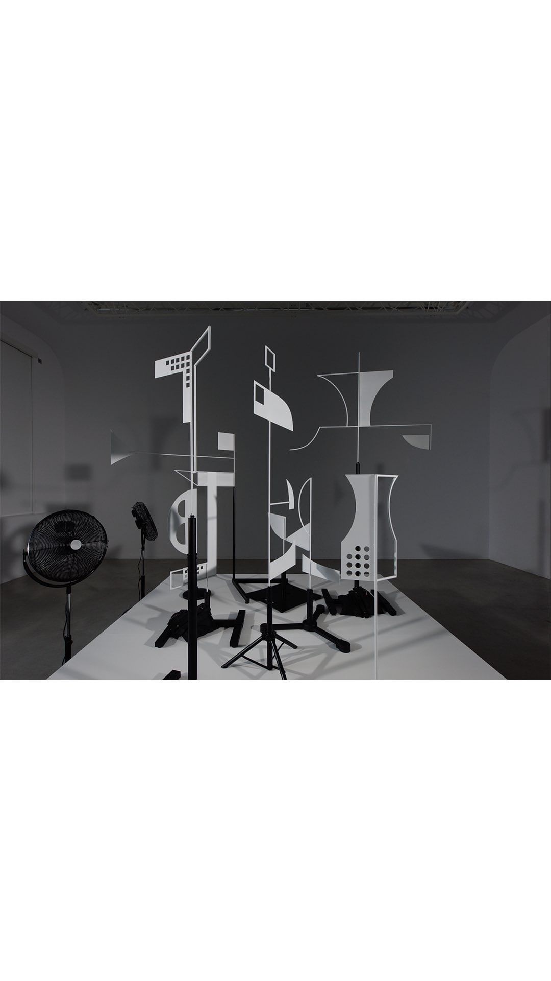 Monochromatic art installation featuring black pedestals and white geometric shapes against a grey wall in a bright photo studio.