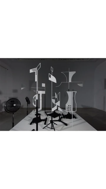 Monochromatic art installation featuring black pedestals and white geometric shapes against a grey wall in a bright photo studio.