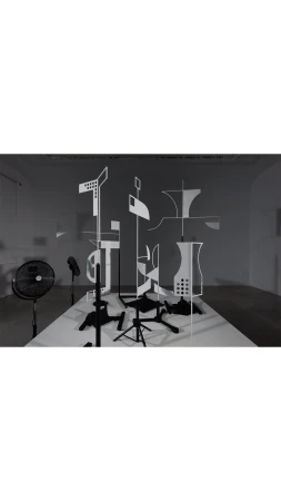 Monochromatic art installation featuring black pedestals and white geometric shapes against a grey wall in a bright photo studio.