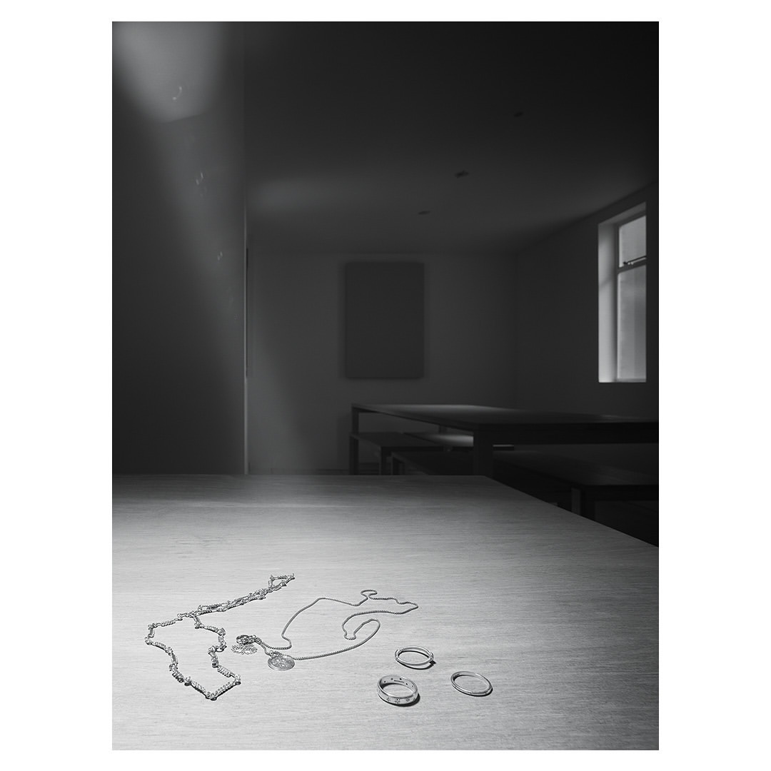 Silver jewellery items including chains and rings arranged on a wooden tabletop in a dimly lit room photographed by Dan Tobin Smith.