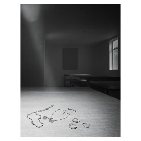 Silver jewellery items including chains and rings arranged on a wooden tabletop in a dimly lit room photographed by Dan Tobin Smith.