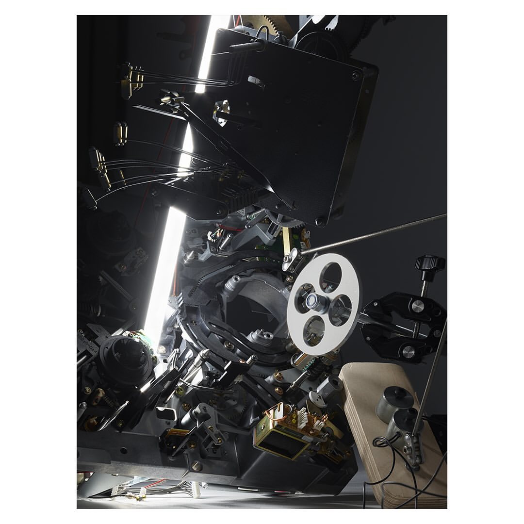 Close-up of a complex film projector mechanism featuring intricate gears, a film reel, and reflective surfaces, highlighting its technical design.