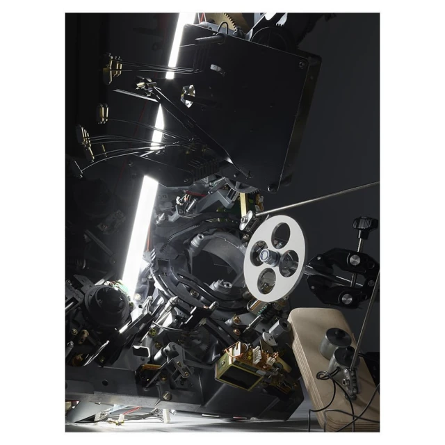 Close-up of a complex film projector mechanism featuring intricate gears, a film reel, and reflective surfaces, highlighting its technical design.
