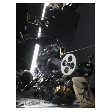 Close-up of a complex film projector mechanism featuring intricate gears, a film reel, and reflective surfaces, highlighting its technical design.