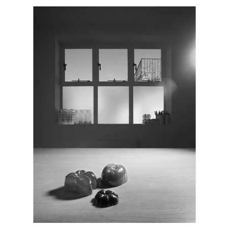 Black and white still life with bell peppers on a table in front of a window providing daylight in an indoor setting.
