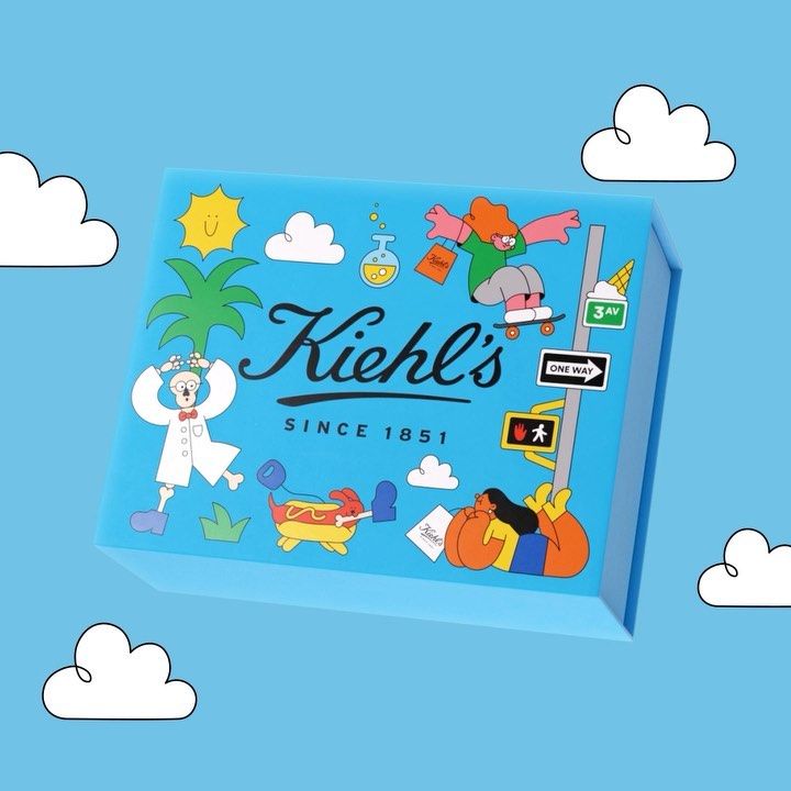 Eye-level shot of a light blue Kiehl's gift box with illustrated cartoon characters, set against a matching light blue background with white clouds.