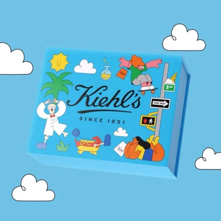 Eye-level shot of a light blue Kiehl's gift box with illustrated cartoon characters, set against a matching light blue background with white clouds.