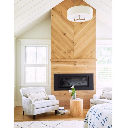 Living room interior with a fireplace framed by light wood paneling, two armchairs, and a white rug with blue patterns.