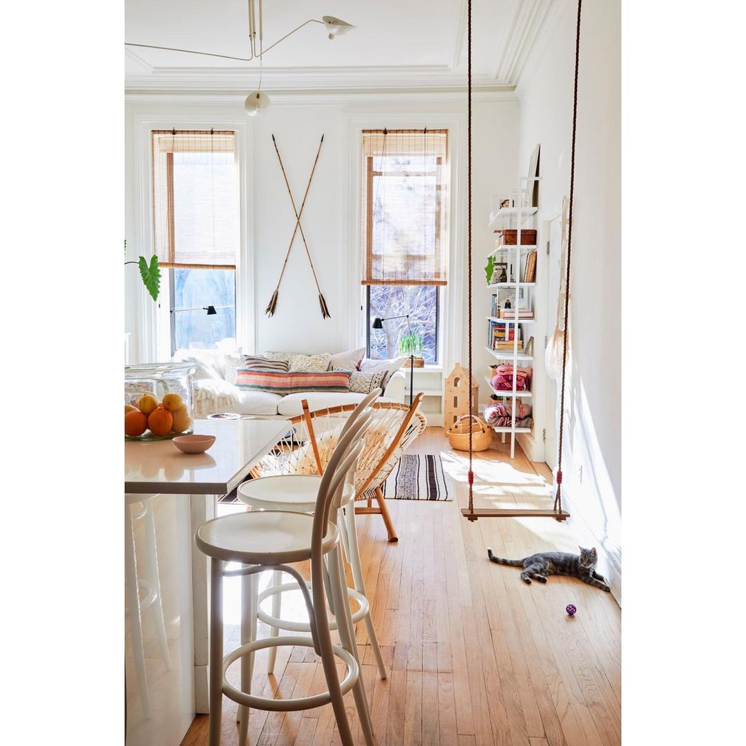 Bright and airy interior shot featuring a swing, shelving, stools, a sofa, and a cat enjoying a sunny day indoors.