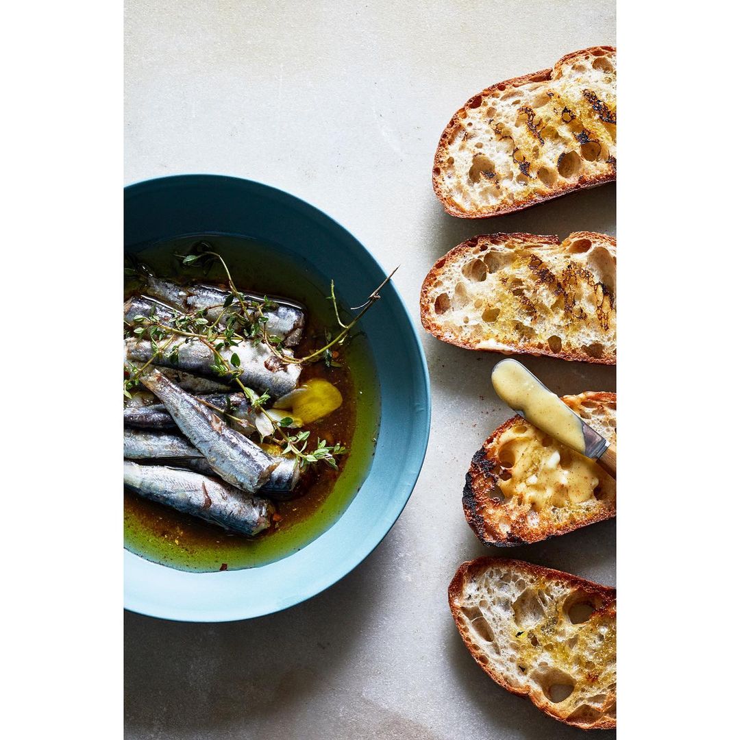 Overhead shot of marinated sardines in a blue bowl, with slices of toasted bread alongside for a flavorful culinary experience.