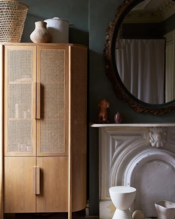Interior shot featuring a light wood cabinet with cane panels, a white fireplace mantle, and a round wall mirror.