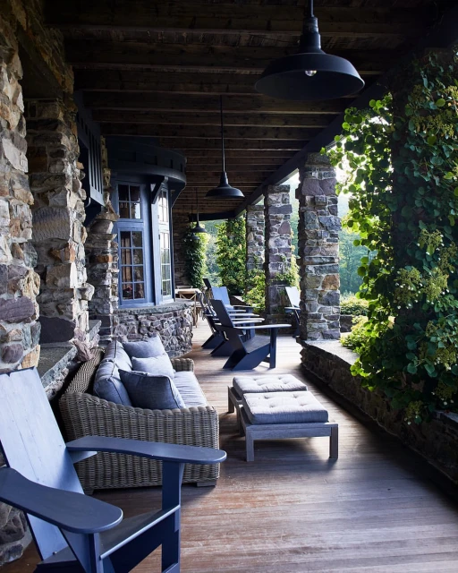 Outdoor porch area featuring stone columns, wicker furniture, wooden floors and overhead lighting fixtures with a view of greenery.