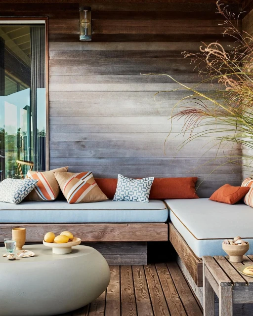 Corner seating area with cushions on wooden platform, side tables with bowls and snacks, oval coffee table, and wood-panelled wall.