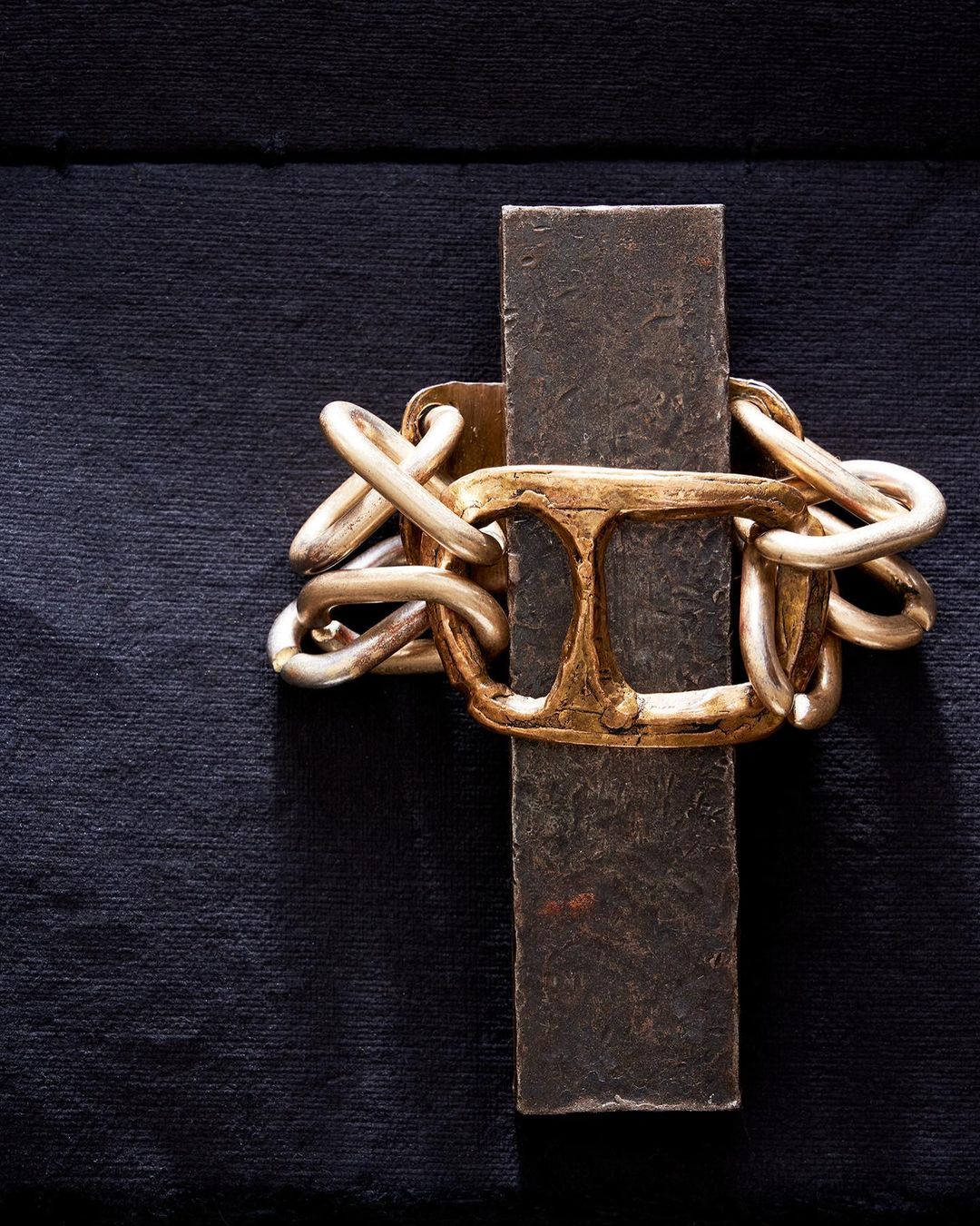 Abstract close-up of a gold chain-link bracelet over a metal bar, set against a dark textured background.