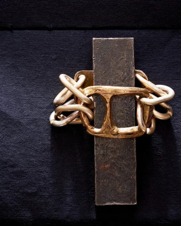 Abstract close-up of a gold chain-link bracelet over a metal bar, set against a dark textured background.