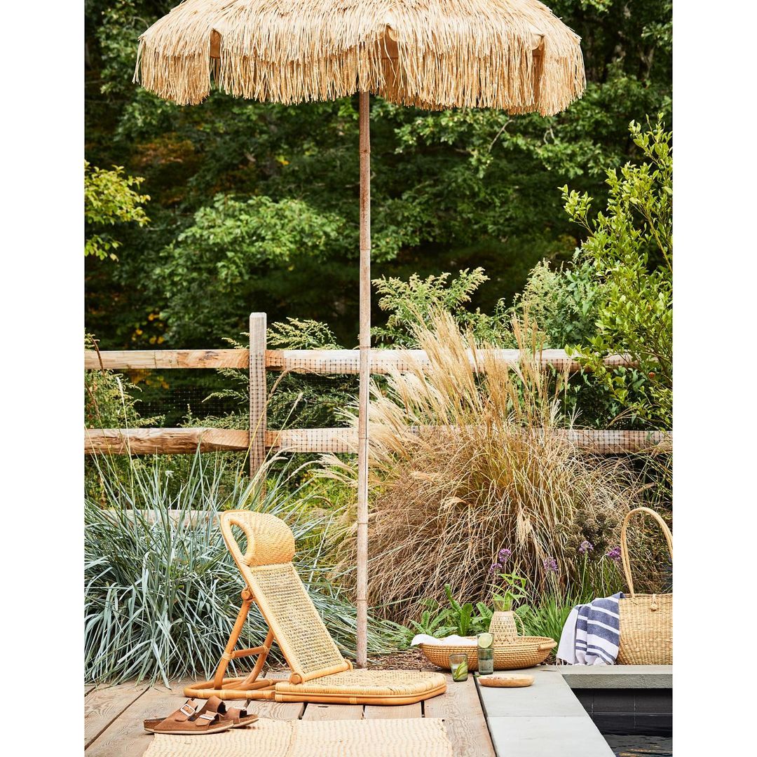 Outdoor poolside setup with a woven beach umbrella, lounge chair, and summer accessories creating a tranquil vacation scene.