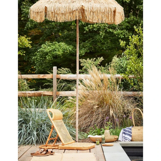 Outdoor poolside setup with a woven beach umbrella, lounge chair, and summer accessories creating a tranquil vacation scene.