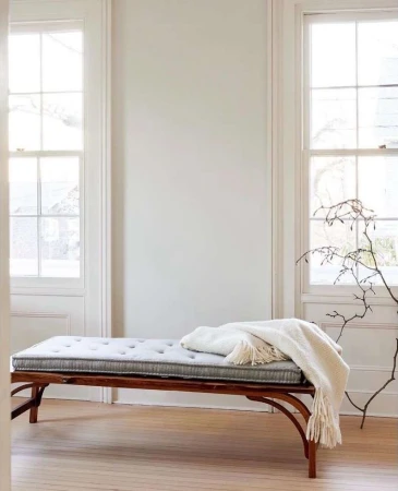 Interior of room featuring a daybed with a gray cushion and a white blanket, set against a backdrop of white walls and windows.