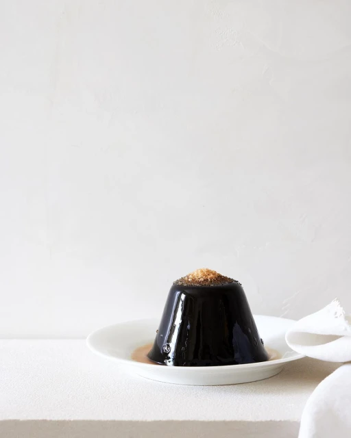 Elegant black jelly dessert topped with brown sugar, served on a white plate with a cloth napkin, against a muted white background.