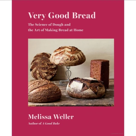 Eye-level product shot of a cookbook called Very Good Bread on a fuchsia background featuring various loaves of bread on a wooden surface.