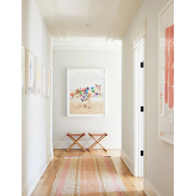 Hallway interior with a framed art print of an animal decorated with colorful pompoms hanging above two wooden folding stools.