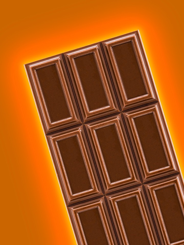 Close-up of a dark chocolate bar on a warm orange background, showing detailed texture and individual sections of the confection.