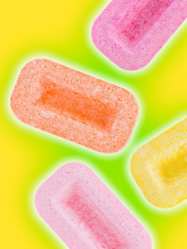 Close-up of colorful, rectangular gummy candy pieces in pink, orange, and yellow on a bright yellow-green background with a soft glow.
