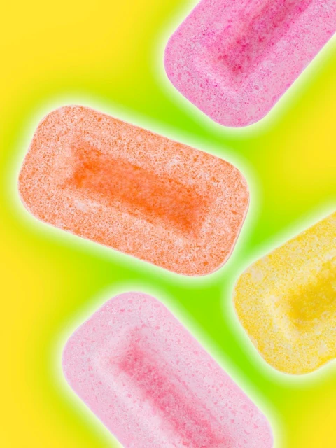 Close-up of colorful, rectangular gummy candy pieces in pink, orange, and yellow on a bright yellow-green background with a soft glow.