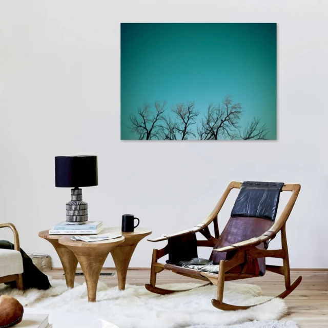 Interior view with mid-century modern rocking chair, sculptural side table with lamp, and a large blue-toned artwork featuring bare trees.