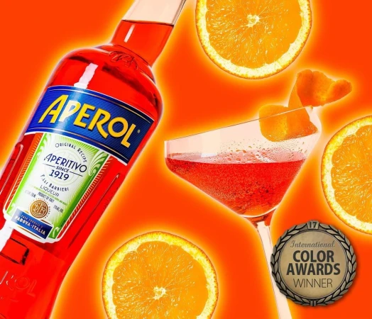 Bottle of Aperol with a cocktail in a glass and orange slices on an orange background. Drink advertisement with International Color Awards Winner.