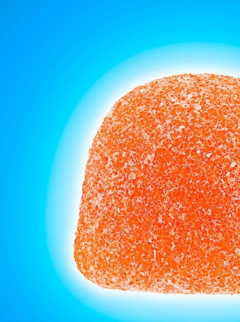 Close-up of a hemispherical orange gummy candy coated in sugar crystals against a vibrant blue gradient backdrop.
