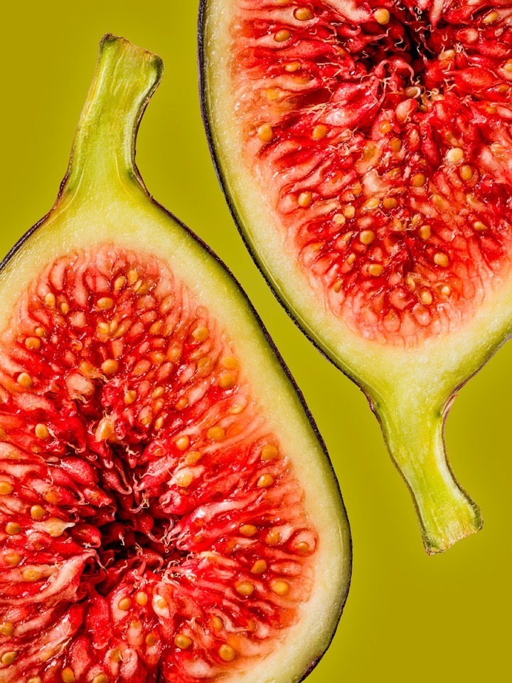 Two fig halves are shown in close-up with the fruit's red interior and pale outer flesh, set against a muted chartreuse background.