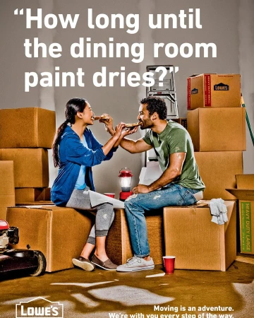 Couple sitting on moving boxes sharing pizza; Lowe's moving ad shows the lighter side of moving day; indoor home shot with moving supplies.