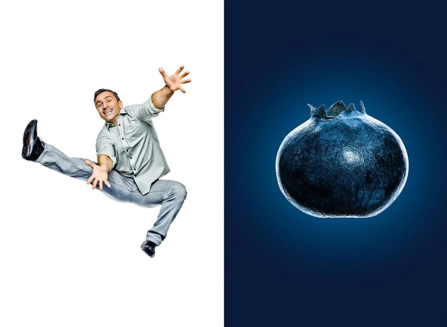 Man in mid-air pose next to a single blueberry against a blue background, contrasting action and macro fruit photography.