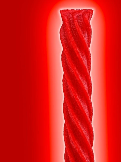 Close-up studio shot of a single red licorice twist against a bright red background with central lighting.
